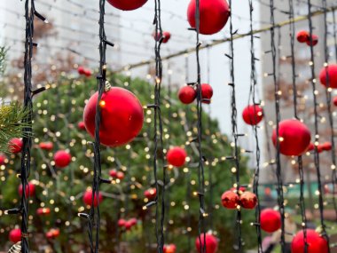 Peri ışıkları arasında asılı duran kırmızı Noel süslerine yakından bakın. Tatil sokak dekorasyonu, kış kutlaması ve coşkulu bir ortam..
