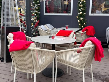 Kış terasında kırmızı battaniyeli yuvarlak kafe masası. Konforlu Noel manzarası, açık hava koltukları ve şenlikli mevsim atmosferi..