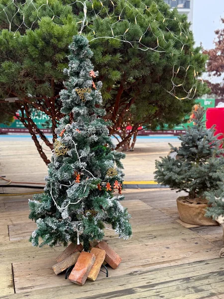 Tahta terasta süsleri olan küçük buzlu Noel ağacı. Minimum tatil dekoru, rahat kış ayarı ve mevsimlik açık hava tasarımı.