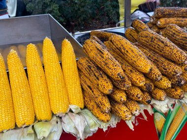 Izgara ve haşlanmış mısır koçanları satılık bir sokak yemeği standında sergileniyor. Yerel mutfak, açık hava atıştırma ve basit mevsimsel malzemeler etrafında toplanmış geleneksel sokak yemekleri kültürü.