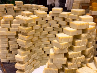 Katmanlı sıra halinde dizilmiş nötr tonlu sabun çubukları desenli bir duvar görüntüsü oluşturuyor. Minimalist cilt bakımı, el yapımı üretim ve saflığı, rutini ve günlük özbakımları vurgulayan düzenli sunum