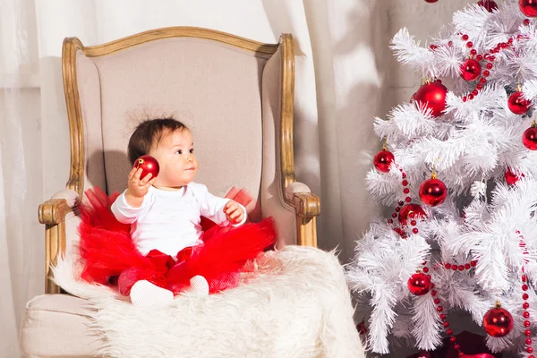 Μικρό κορίτσι που κάθεται σε μια καρέκλα κοντά το χριστουγεννιάτικο δέντρο — Φωτογραφία Αρχείου