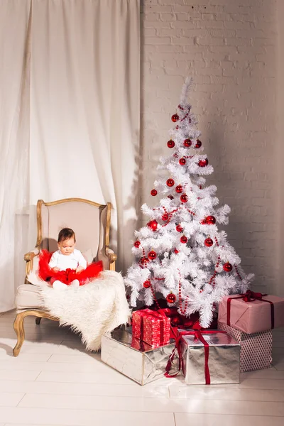 Menina senta-se em uma cadeira perto da árvore de Natal — Fotografia de Stock