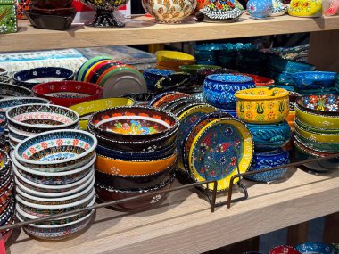 Dekoratif Türk seramik kaseleri ve tabakları esnaf dükkanında sergileniyor. Geleneksel çömlekçilik, işlevsel tasarım, kültürel işçilik, renkli sofra takımı, el yapımı üretim ve günlük ev yapımı estetik.