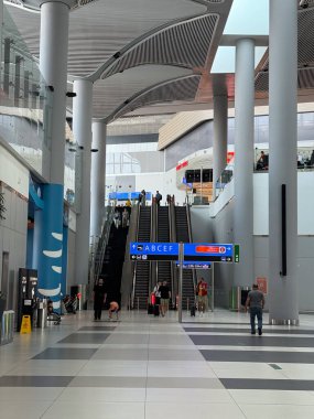 Geniş havaalanı içi yürüyen merdiven ve yön tabelalarıyla dolu. Yolcu seyrüsefer, dikey dolaşım, mimari ölçek ve ulaşım merkezi içinde organize hareket.