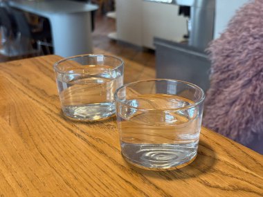 Ahşap kafe masasında iki bardak su. Sosyal yemek ortamında basitlik, susuzluk ve sakin atmosfer