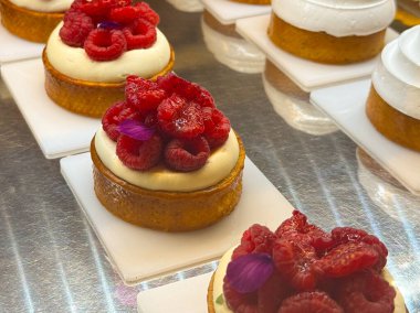 Beyaz kremalı yuvarlak pastalar ve beyaz tabaklara yerleştirilmiş kırmızı böğürtlenlerle süslenmiş pastalar. Pastane krem, renk ve zanaat birleştirme görüntüsü.