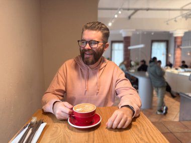 Modern kafede latte içen bir adam. Günlük rahatlama, sabah ritüeli ve şehir yaşam tarzında rahat kahve kültürü.