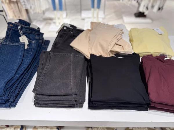 Farklı renk ve boyutlarda katlanmış pantolonlar bir perakende masasında düzgünce düzenlenir. Modern yaşam tarzı endüstrisinde tüketici talebi, ticaret, tekstil ticareti ve moda alışveriş eğilimleri