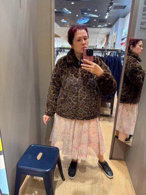 Soyunma odasında pastel tül etekli sahte kürk ceket deneyen bir kadın. Cesur hayvan modeliyle yumuşak romantik dokuyu birleştiren moda deneyi.