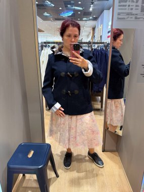 Depoda çiçekli eteklerin üstüne düğme takan donanma spor ceketi giyen bir kadın. Konfor, yapı ve mevsimsel zarafeti ifade eden klasik sonbahar dış giysisi.