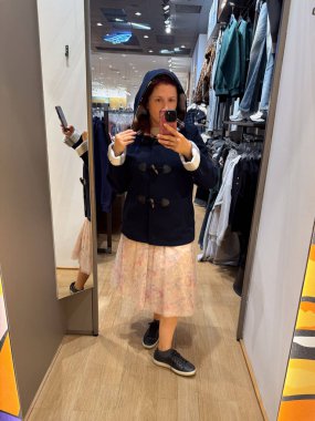 Giyinme odasında kapüşonlu donanma ceketi deneyen bir kadın. Sıcaklık konforu, sadeliği ve mevsimlik cazibeyi sembolize eder