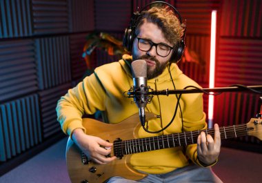 Gitarlı bir kayıt stüdyosunda şarkı söyleyen erkek vokalist. Erkek şarkıcı bir şarkı söylüyor ve gitar çalıyor. Ses kaydı ve müzik akışı kavramı