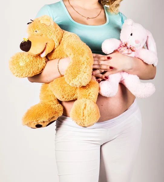Zwangere vrouw met speelgoed op haar buik — Stockfoto