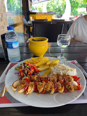 Izgara tavuk şişi, yanında patates kızartması ve kafeterya masasında taze salata. Günlük yemek, açık hava yemek, seyahat yemeği deneyimi ve günlük restoran yaşam tarzı..