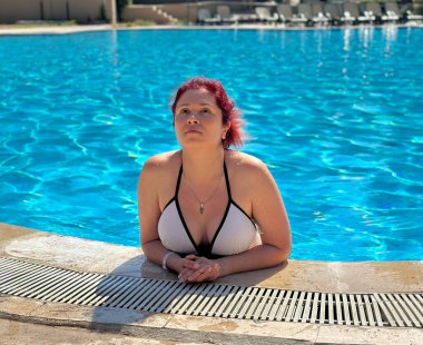 Güneş ışığı altında havuz kenarına yaslanan bir kadın. Yaz tatili, tatil, dinlenme, su keyfi ve sakin bir tatil anı..