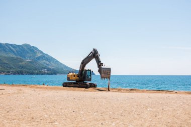 Kazıcı deniz kenarında bir sahil bölgesinde çalışıyor. Altyapı hazırlığı, insan müdahalesi ve deniz kenarı gelişimi içindeki manzara değişimi