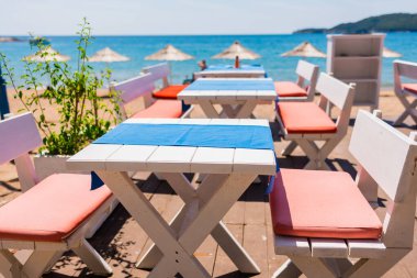 Sahildeki kafe masasında denize bakan renkli yastıklar var. Rahat deniz kenarı yemekleri, sakin eğlence ritmi ve kıyı sadeliğiyle şekillenen tatil atmosferi.