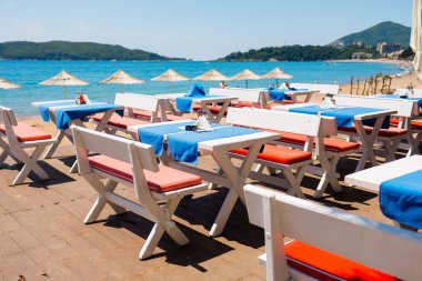 Sahil kenarındaki kafe masaları kıyı şeridi boyunca dizilmiş. Sahildeki yemek saatlerinden önce düzen, tekrarlama ve konukseverlik ortamı.