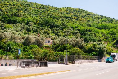 Tepe manzaralı güneşli bir cadde. Kentsel yaşam, doğa entegrasyonu ve kıyı bölgesinde rahat bir Akdeniz yaşam tarzı.