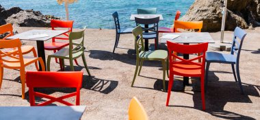 Deniz kenarı terasında renkli sandalyeler ve su kenarında katlanmış şemsiyeler. Sahil kafesi, yaz tatili ve tatil konsepti.