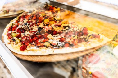 Camın arkasında renkli meyveli tatlı pizzası. Tatlı malzemeler, gurme aperatifler ve taze çilek, muz dilimleri ve erimiş çikolatalı hoşgörülü sokak yemekleri.