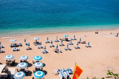 Adriyatik Denizi kıyısında şemsiyeli ve şezlonglu organize çakıl taşı plajı. Karadağ 'ın Budva kentinde yaz turizmi, kıyı konforu, tatil rutini ve deniz kenarındaki rahat yaşam tarzı.