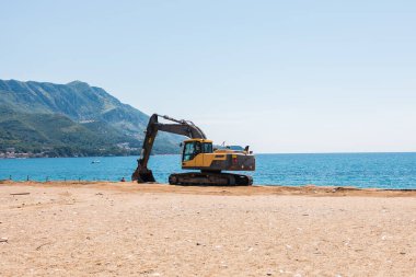 Kazıcı deniz kenarında bir sahil bölgesinde çalışıyor. Altyapı hazırlığı, insan müdahalesi ve deniz kenarı gelişimi içindeki manzara değişimi