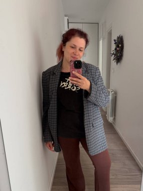 Bir kadın, evde ekose ceketli, günlük kıyafetleriyle selfie çekiyor. Orijinalliğin, konforun ve modern günlük kendini ifade etmenin temsili