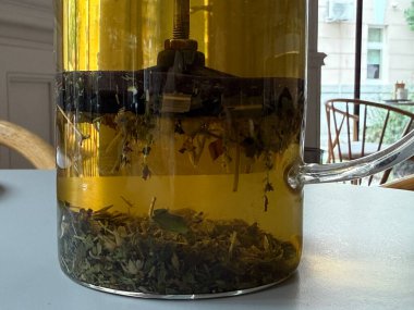 Cam çaydanlıkta demlenen bitki çayının yakın çekimi. Doğal malzemeler, sağlık ve yavaş yaşam tarzı.