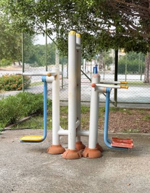 Parkın yanındaki tenis kortunun yanında pedalları ve barları olan açık hava eğitim makinesi. Spor, hareket ve sağlık günlük yaşam tarzında toplumsal etkinlik, güç ve sağlık gösteriyor.