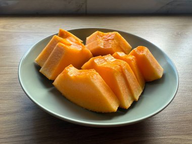 Tahta bir masada seramik bir tabakta sergilenmiş taze dilimlenmiş kavun. Sağlıklı beslenme, yaz içeceği, ve doğal ışıkta minimum gıda tasarımı..