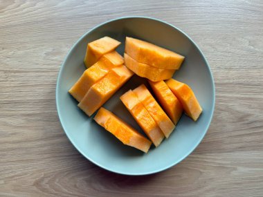 Tahta bir masada seramik bir tabakta sergilenmiş taze dilimlenmiş kavun. Sağlıklı beslenme, yaz içeceği, ve doğal ışıkta minimum gıda tasarımı..