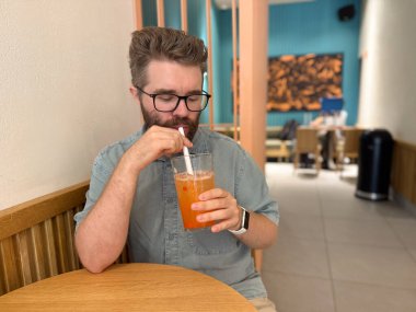 Adam kafenin içinde samanla buzlu meyve çayı içiyor. Kentsel yaşam tarzı, dinlenme molası ve gündelik içki anlarıyla modern yemek deneyimi..