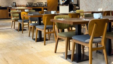 Ahşap masaları ve döşeli sandalyeleri olan boş bir otel restoranı. Konukseverlik hizmeti, kahvaltı düzenleme ve mobilya düzeni ve modern kafe tasarımı yoluyla iç konfor.