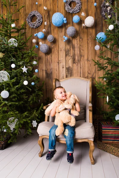 Jongen zittend in de stoel in de buurt van de kerstboom — Stockfoto