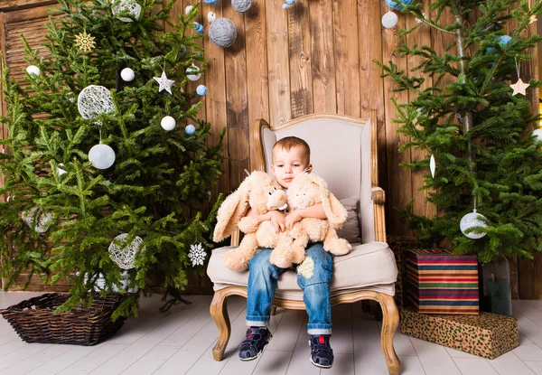 Αγόρι κάθεται στην καρέκλα κοντά χριστουγεννιάτικο δέντρο — Φωτογραφία Αρχείου