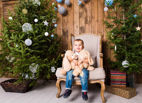 Αγόρι κάθεται στην καρέκλα κοντά χριστουγεννιάτικο δέντρο — Φωτογραφία Αρχείου