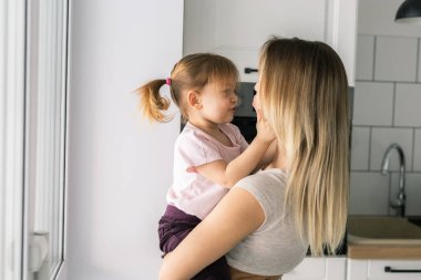 Anne, küçük kızıyla birlikte mutfağın içinde gülüyor. Aile sevinci, duygusal yakınlık ve günlük hayatta neşeli bir bağ.