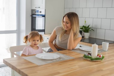 Anne, küçük kızıyla birlikte mutfağın içinde gülüyor. Aile sevinci, duygusal yakınlık ve günlük hayatta neşeli bir bağ.