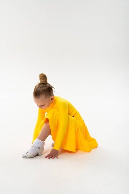 Koklear implantı olan sarı dans elbisesi giyen, ayakkabılarını ayarlayan bir kız. Pediatrik fizik tedavi, işitme desteği ve sanatsal hareket yoluyla spor gelişimi.