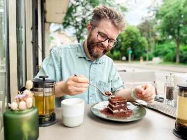 Açık kafede elinde çaydanlık ve fincanla pasta yiyen bir adam. Günlük rahatlama ve otantik yemek zevkinin yaşam tarzı ve boş yemek deneyimi