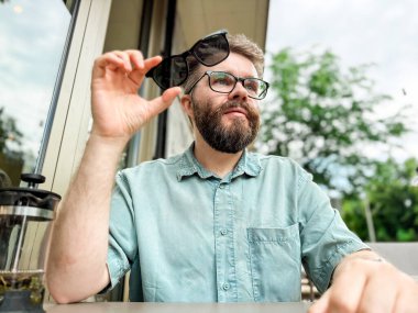 Güneş gözlüklerinde manyetik şarjör olan gözlük. Dışarıdaki kafe masasında güneş gözlüğü takan bir adam gülümsüyor..