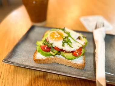 Samimi bir kafede seramik tabakta servis edilen yumurtalı avokado tostu. Sağlıklı kahvaltı ve dengeli beslenme.