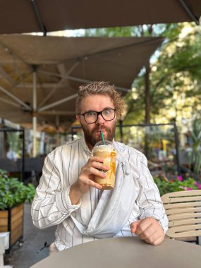 Adam açık kafede karamel frappe içiyor. Sosyal bağlantı, yaz tatili, şehir eğlencesi ve olumlu duygu..
