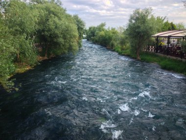 Ağaçlar ve teras kafeler arasında akan nehir. Doğal rahatlama, seyahat yeri ve eğlence konsepti