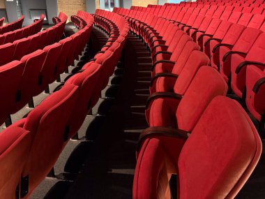 Sıcak ışıklandırmalı kırmızı tiyatro koltukları. Mimari ritim, simetri ve kültürel beklenti sakin iç geometriye yansıyor