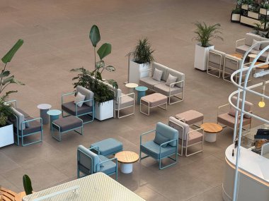 Yeşillik ve pastel koltuklu modern kafe alanı yukarıdan görünüyor. Rahatlama, sosyal toplantılar, iç tasarım, rahat atmosfer ve çağdaş konukseverlik.