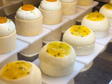 Pasta vitrinine konmuş mango jöleli yuvarlak kremalı kekler. Tazeliği, yumuşaklığı ve pastaneyi sembolize eden tatlı sunumu