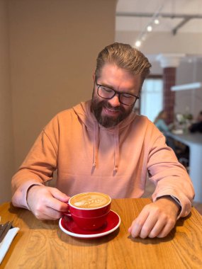 Modern kafede latte içen bir adam. Günlük rahatlama, sabah ritüeli ve şehir yaşam tarzında rahat kahve kültürü.
